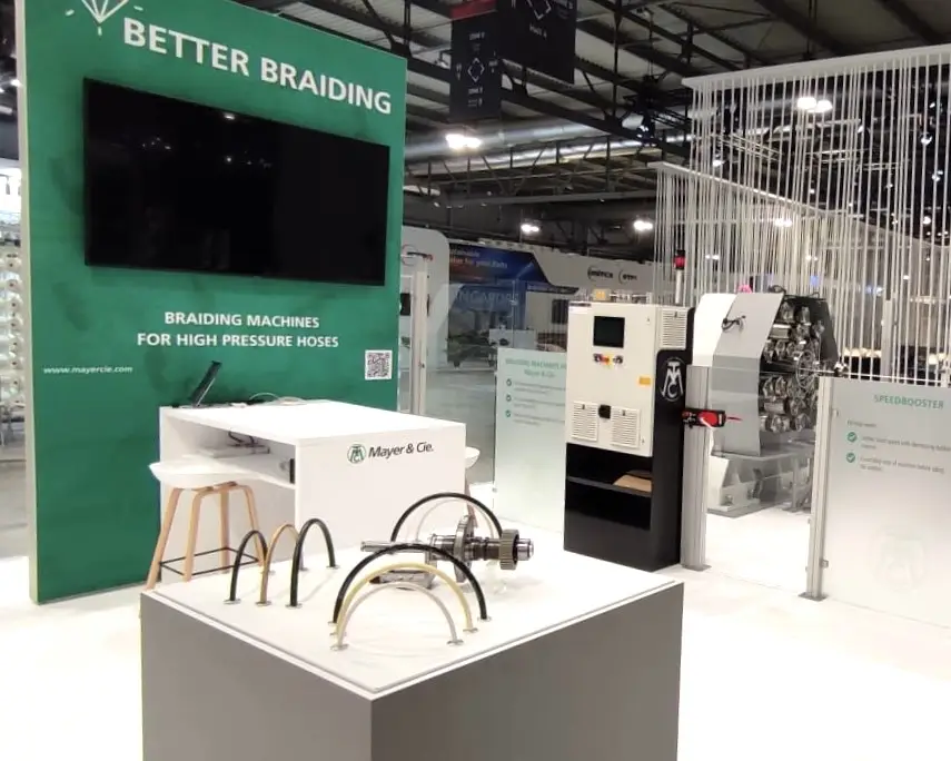 Großer Doppelstock-Messestand mit einer Fläche von 400 qm und einer zweiten Ebene von 100 qm. Offenes, modernes Design mit Glaswänden, großzügigen Ausstellungsflächen und markantem Branding der Firma Mayer & Cie. Der Stand zeigt industrielle Maschinen, informative Displays und Sitzbereiche auf beiden Ebenen. Helle Beleuchtung und klare Strukturen laden Besucher ein.